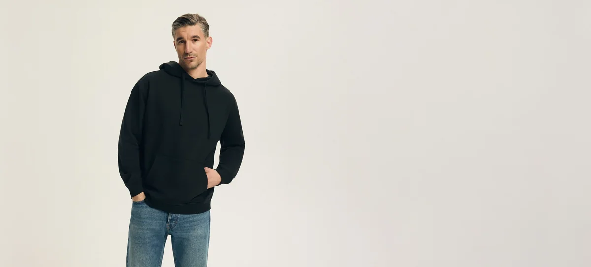Model w ciemnej bluzie Henderson i jasnych jeansach.