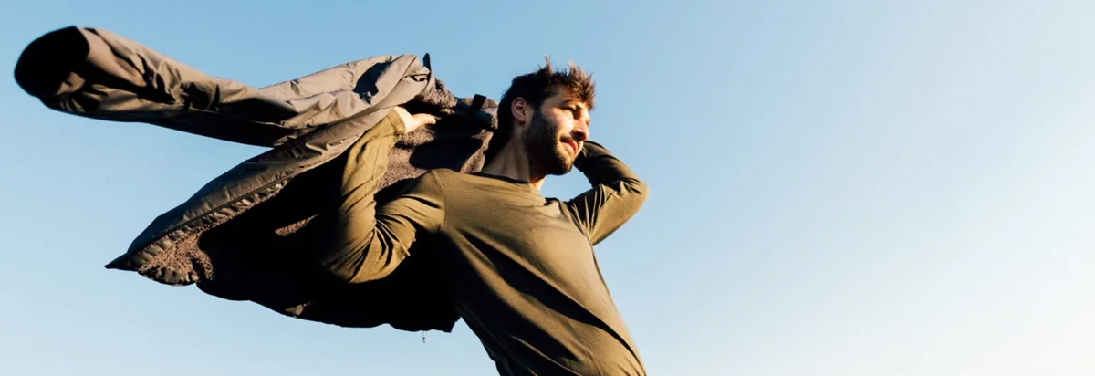 Mężczyzna zakładający kurtkę Jack Wolfskin na tle błękitnego nieba.