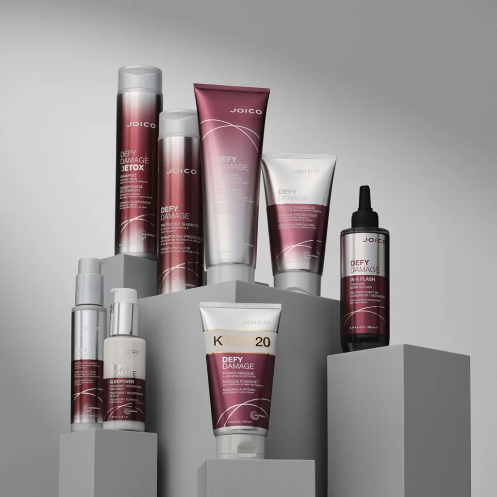 Kosmetyki Joico Defy Damage w bordowych opakowaniach na szarych podestach.