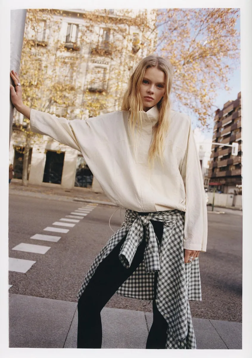 Modelka w jasnym swetrze i wzorzystej spódnicy na ulicy podczas sesji Pull&Bear.