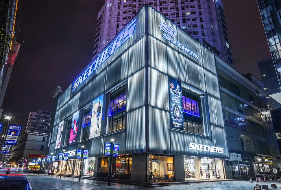 Oświetlona fasada sklepu Skechers na narożniku budynku nocą.