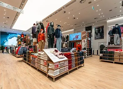 Wnętrze sklepu UNIQLO Wars Sawa Junior ze stołami z odzieżą i manekinami.